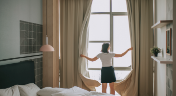 a woman opening curtains in front of a window